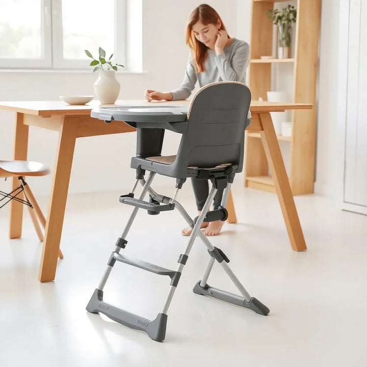 Bärbar barnstol nära matbordet med synlig säkerhetssele och stabil hopfällbar design